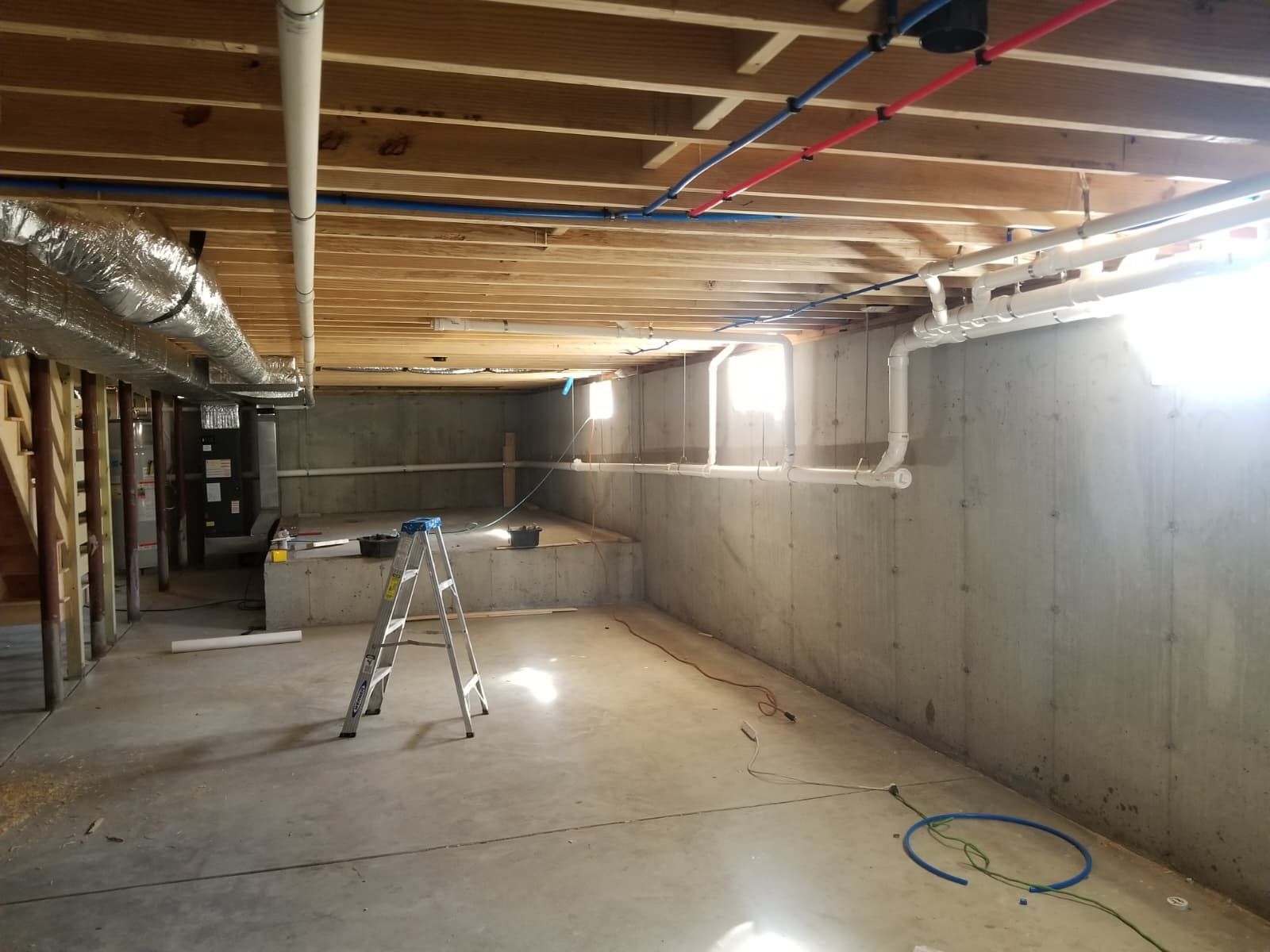 Unfinished basement with concrete walls, exposed ceiling joists, and a step ladder on a bare floor