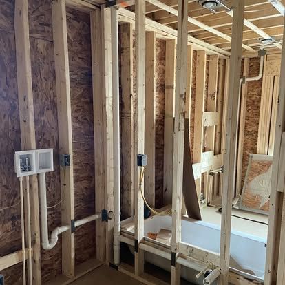 Unfinished bathroom framing with exposed studs, plumbing, and a partially installed bathtub on subfloor.
