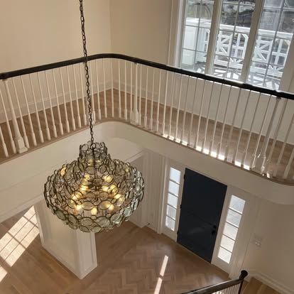 Bright foyer with a large chandelier, white railings, hardwood floor, and staircase landing.