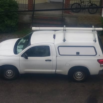 White pickup truck with a canopy and roof rack parked on a street.