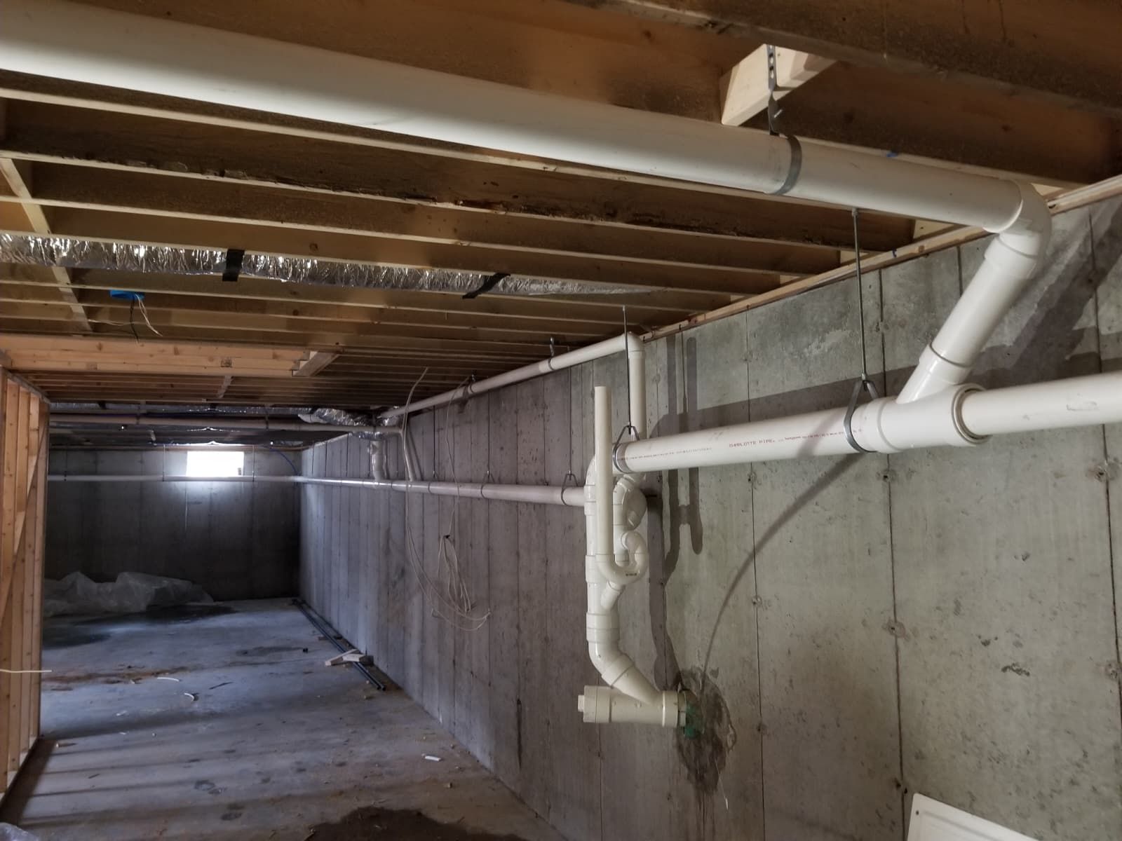 Unfinished basement with exposed joists, concrete walls, and white plumbing pipes along the right side.