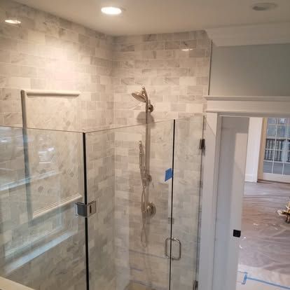 Glass shower enclosure in a tiled bathroom, with chrome fixtures and an open doorway to an adjoining room.