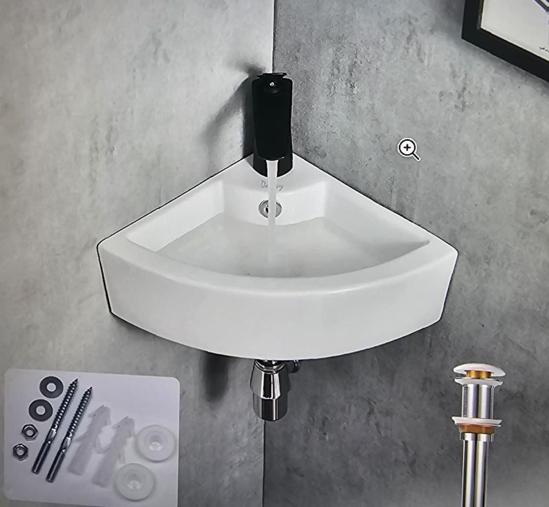 White wall-mounted corner sink with black faucet and soap dispenser on a gray tiled wall.