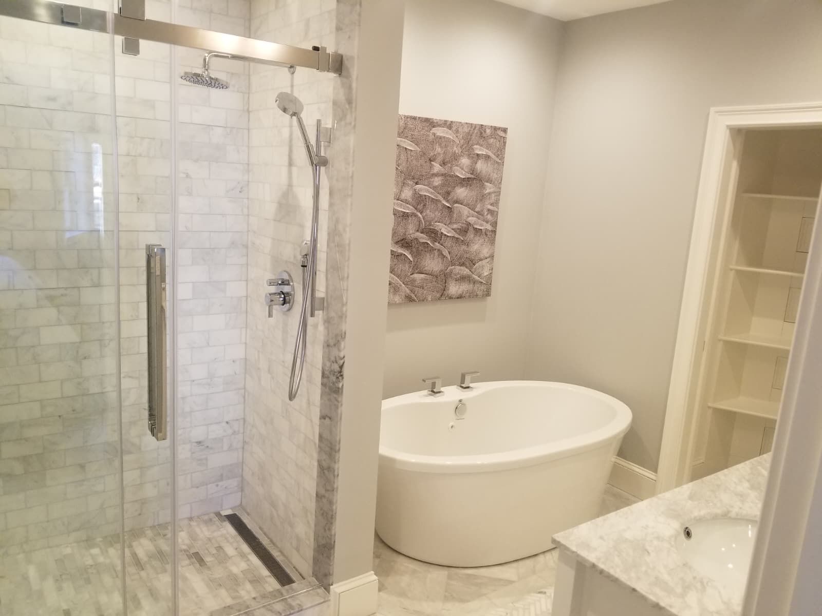 Modern bathroom with glass shower, freestanding tub, marble vanity, and built-in shelving.