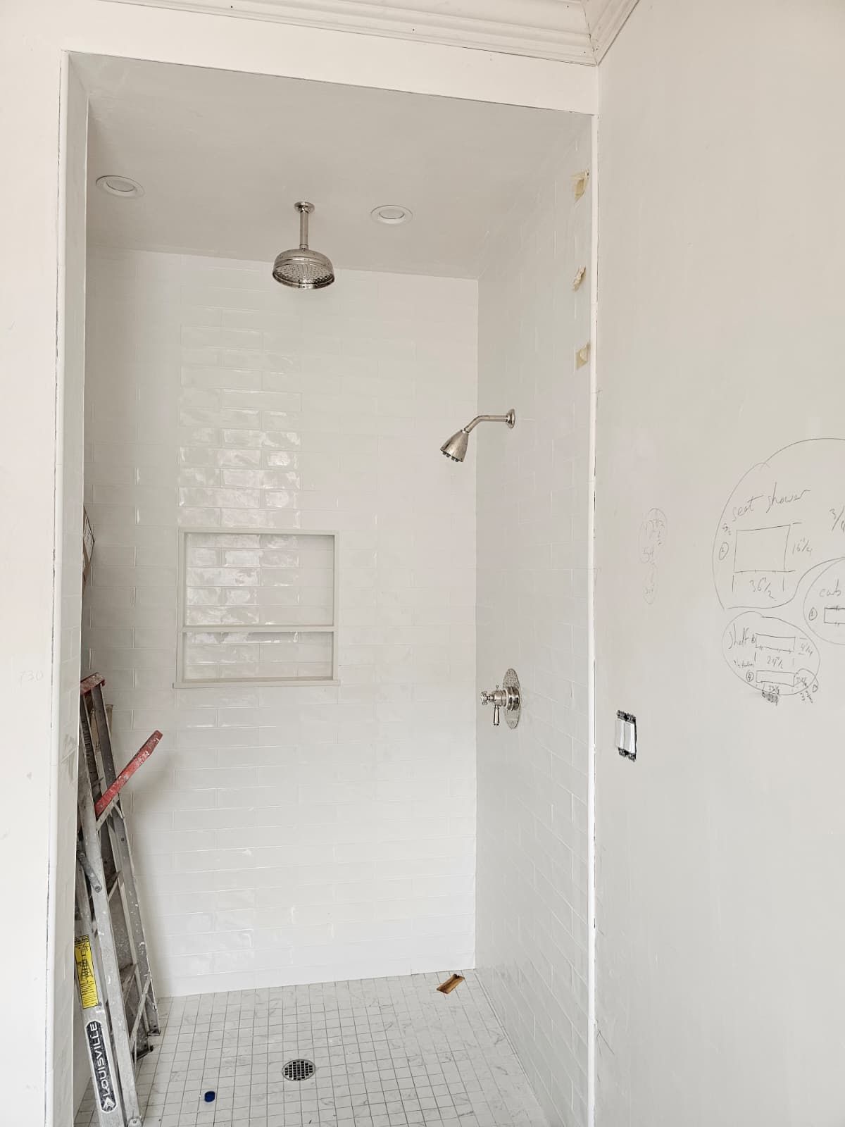 Empty white-tiled shower stall with a small showerhead and built-in shelf.