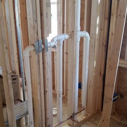 Interior wall framing with white PVC plumbing pipes and drains under construction