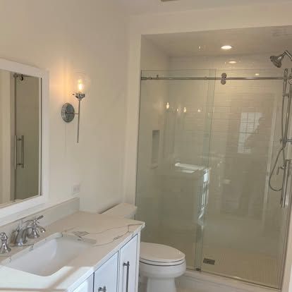 Bright white bathroom with vanity, toilet, and glass-enclosed shower.