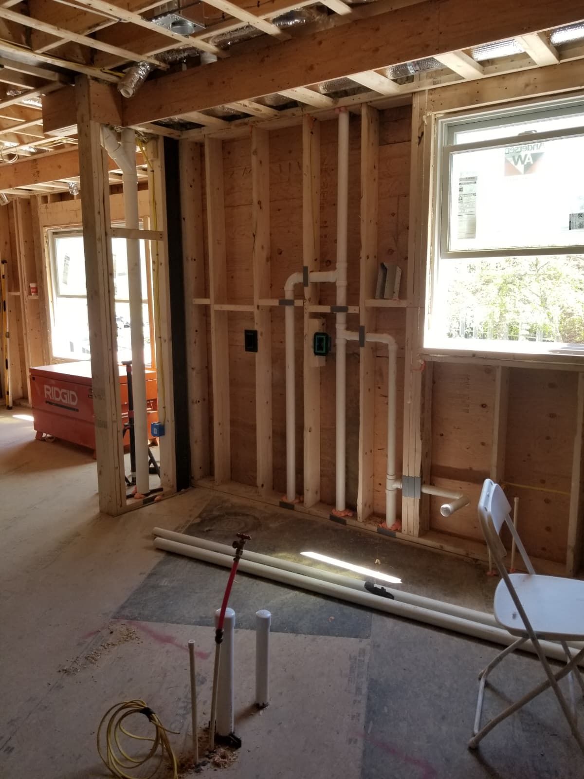 Unfinished room interior with exposed studs, windows, and construction tools on the floor.