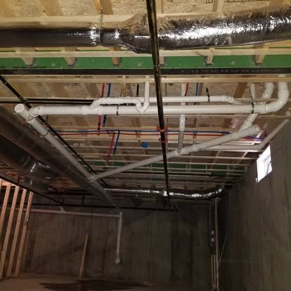 Underground utility room ceiling with exposed pipes, ducts, and wiring above concrete walls