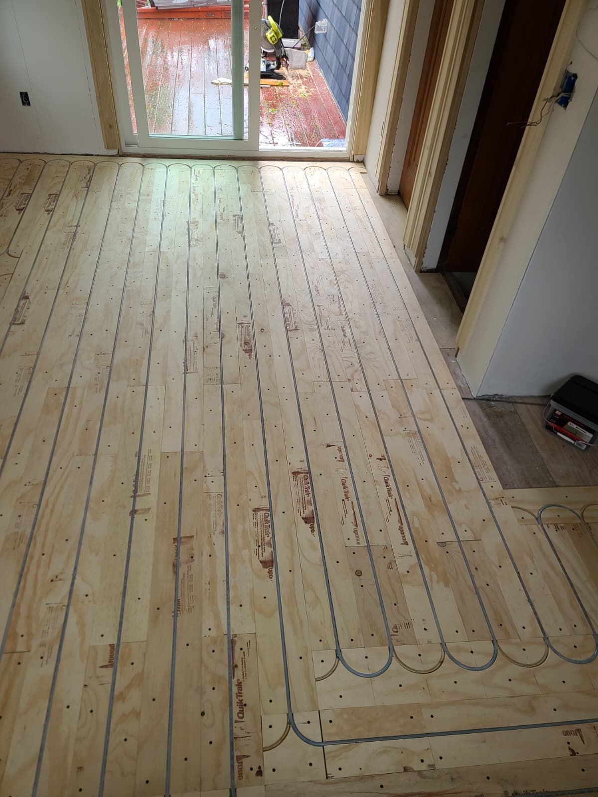 Unfinished wood floor with radiant heating tubing laid in a room near a glass door.