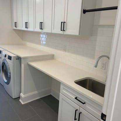 Modern white laundry room with stacked washer and dryer, countertop, sink, and upper cabinets