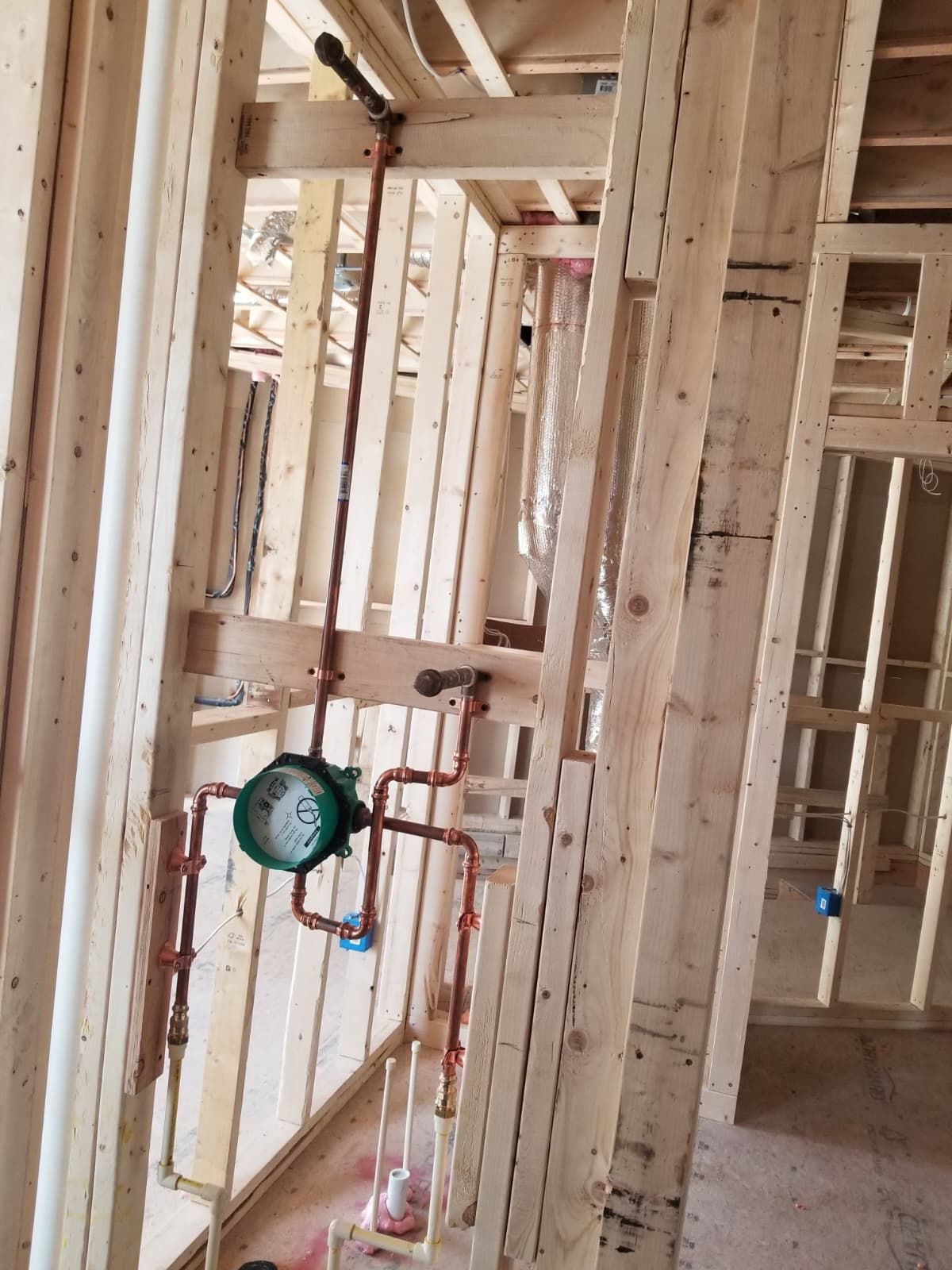 Unfinished wooden house framing with exposed plumbing and a green gauge on a pipe