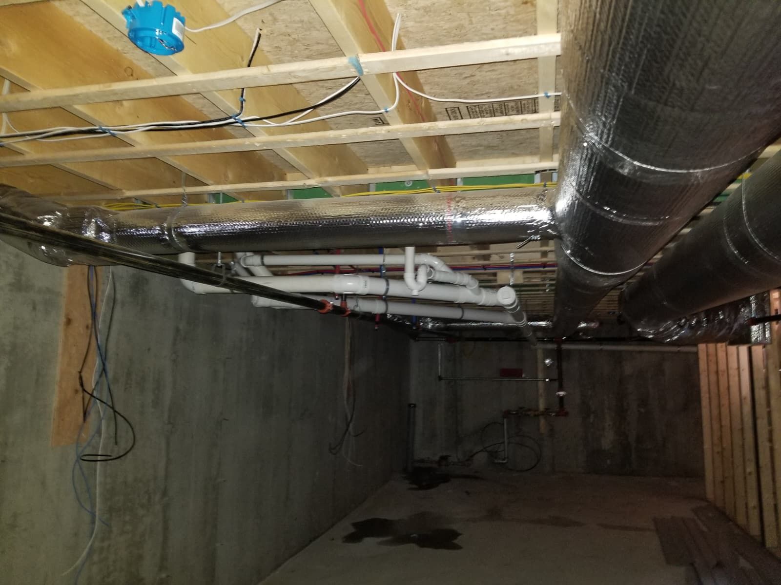Underground tunnel with exposed pipes, ducts, and wiring along concrete walls and ceiling