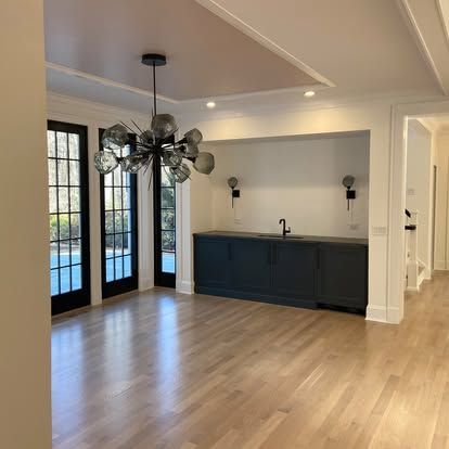 Empty modern room with light wood floors, black-framed doors, and a dark blue built-in cabinet with sink.