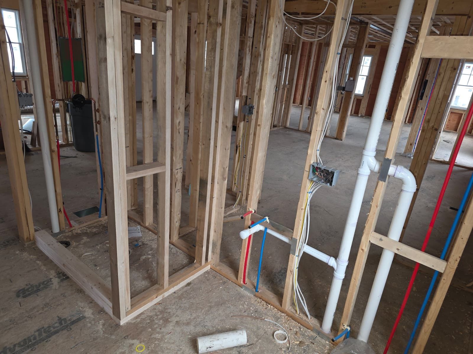 Framed house interior under construction with exposed wood studs and colored plumbing pipes