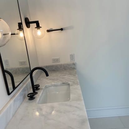 Modern bathroom vanity with marble countertop, black faucet, mirror, and wall sconces
