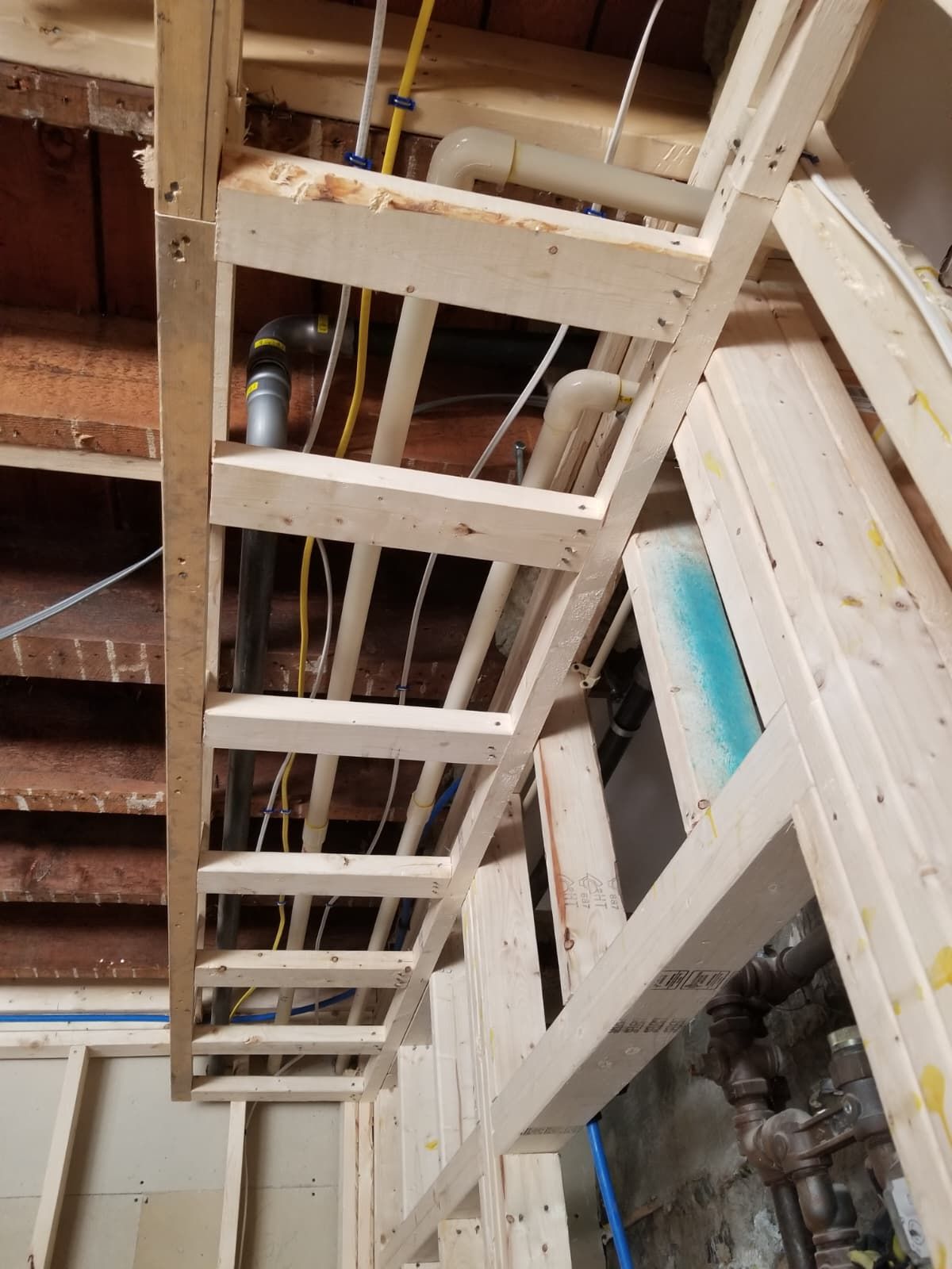 White wooden staircase framing an unfinished interior with exposed beams, pipes, and brick walls