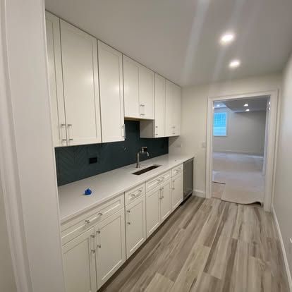 Bright modern galley kitchen with white cabinets, dark backsplash, and wood-look flooring.