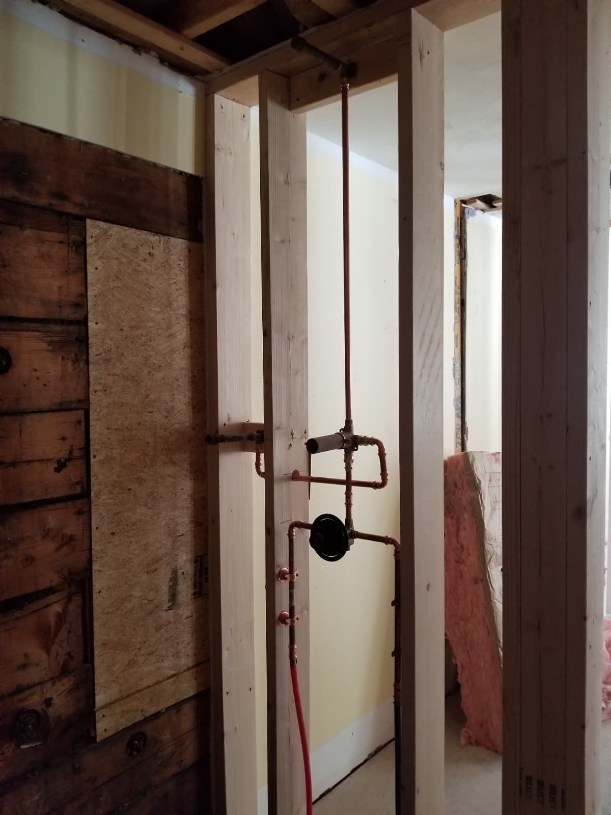 Partially framed room with exposed wood studs, a hanging lock, and a narrow doorway opening to daylight