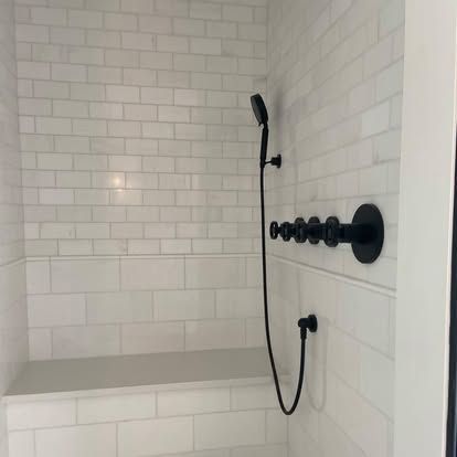 White-tiled shower with built-in bench and matte black handheld showerhead and controls