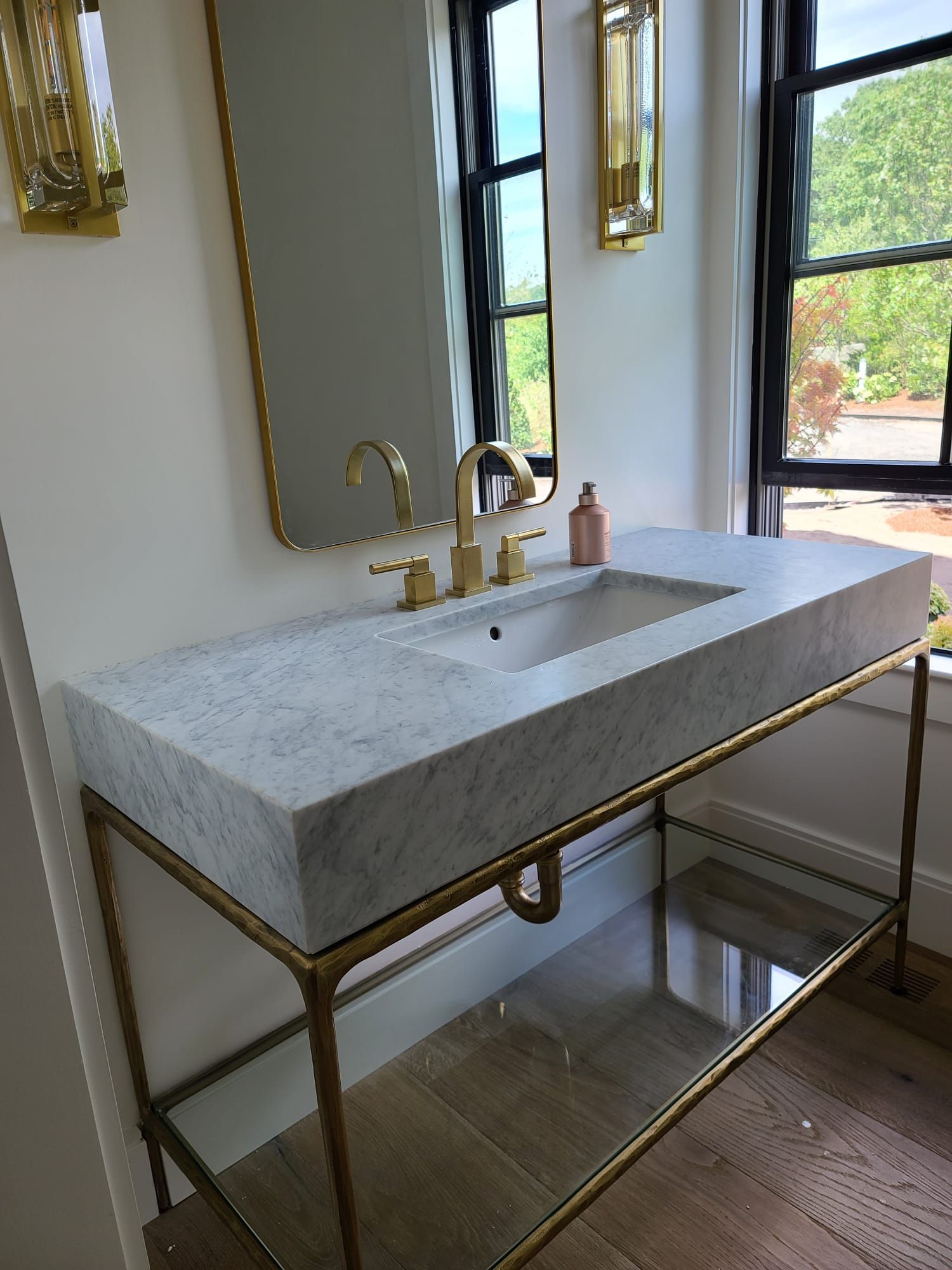 Modern bathroom vanity with stone sink, brass faucet, and mirror beside a window
