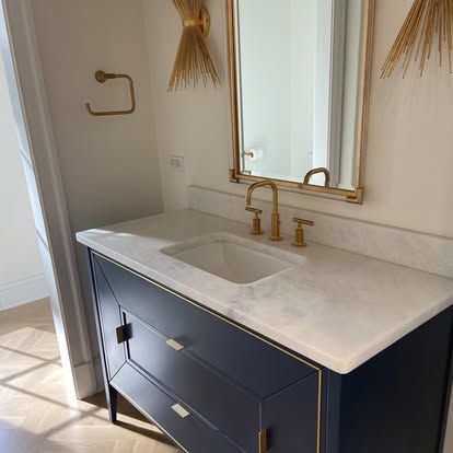 Elegant navy vanity with white countertop, gold fixtures, and mirror in a bright bathroom