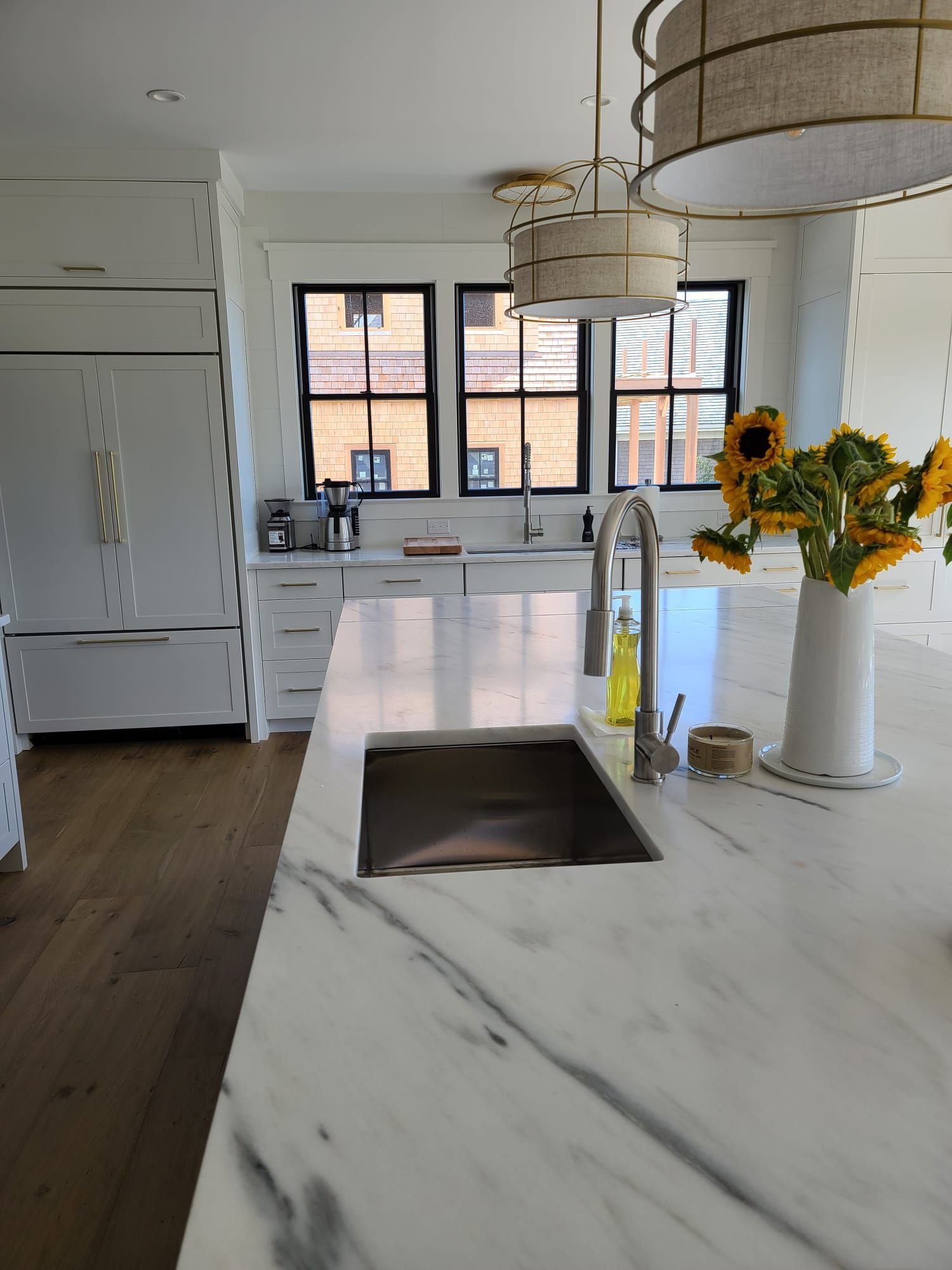 Modern kitchen with white marble island, farmhouse sink, black windows, and sunflowers on the counter