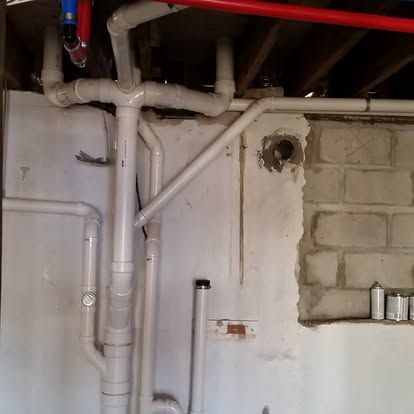 Basement with exposed white pipes and ducts beside an unfinished cinder block wall.