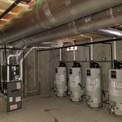 Mechanical room with water heaters, ductwork, and concrete walls in a basement utility space
