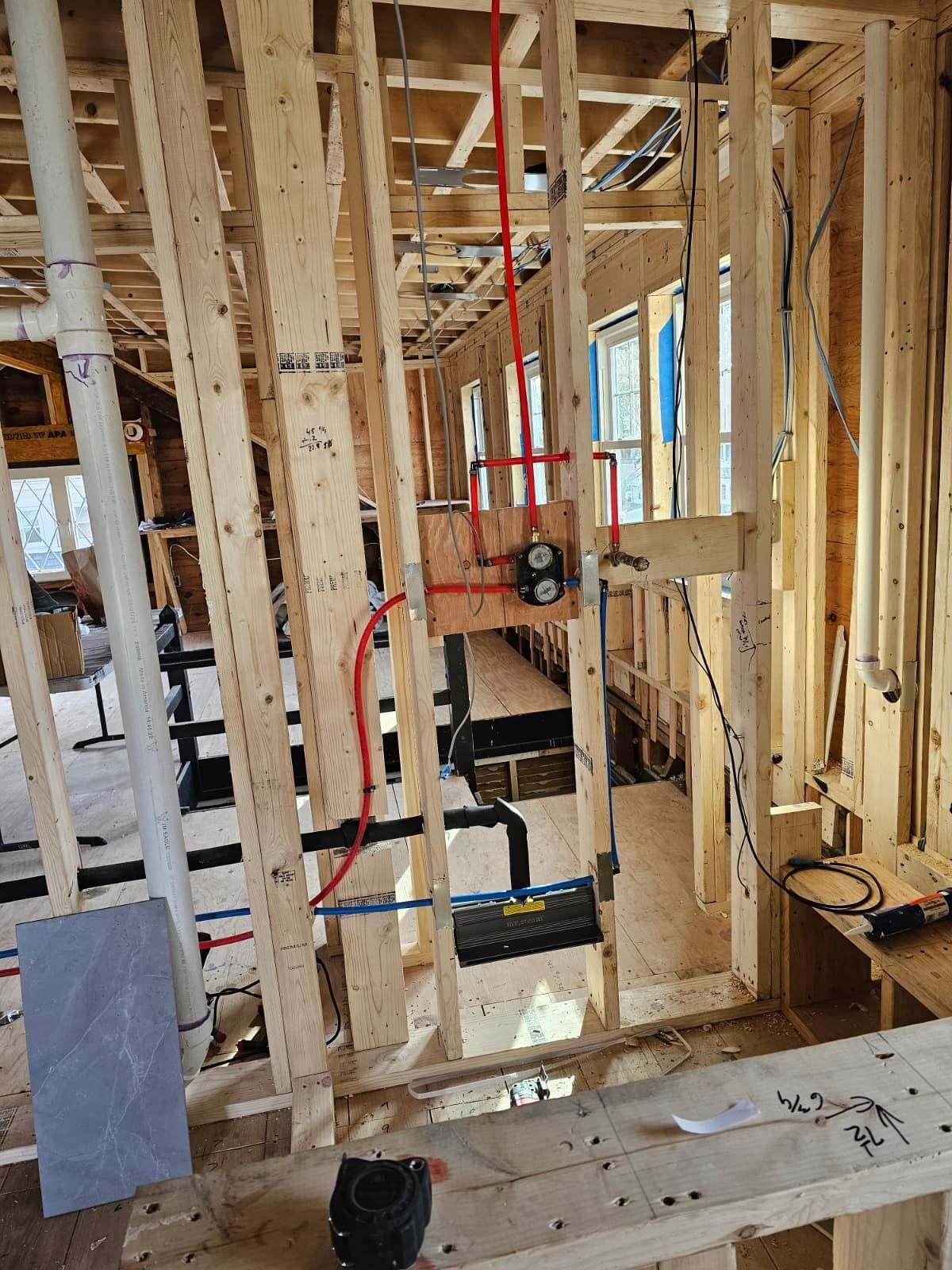 Interior of a wood-framed house under construction with exposed studs, wiring, and tools.