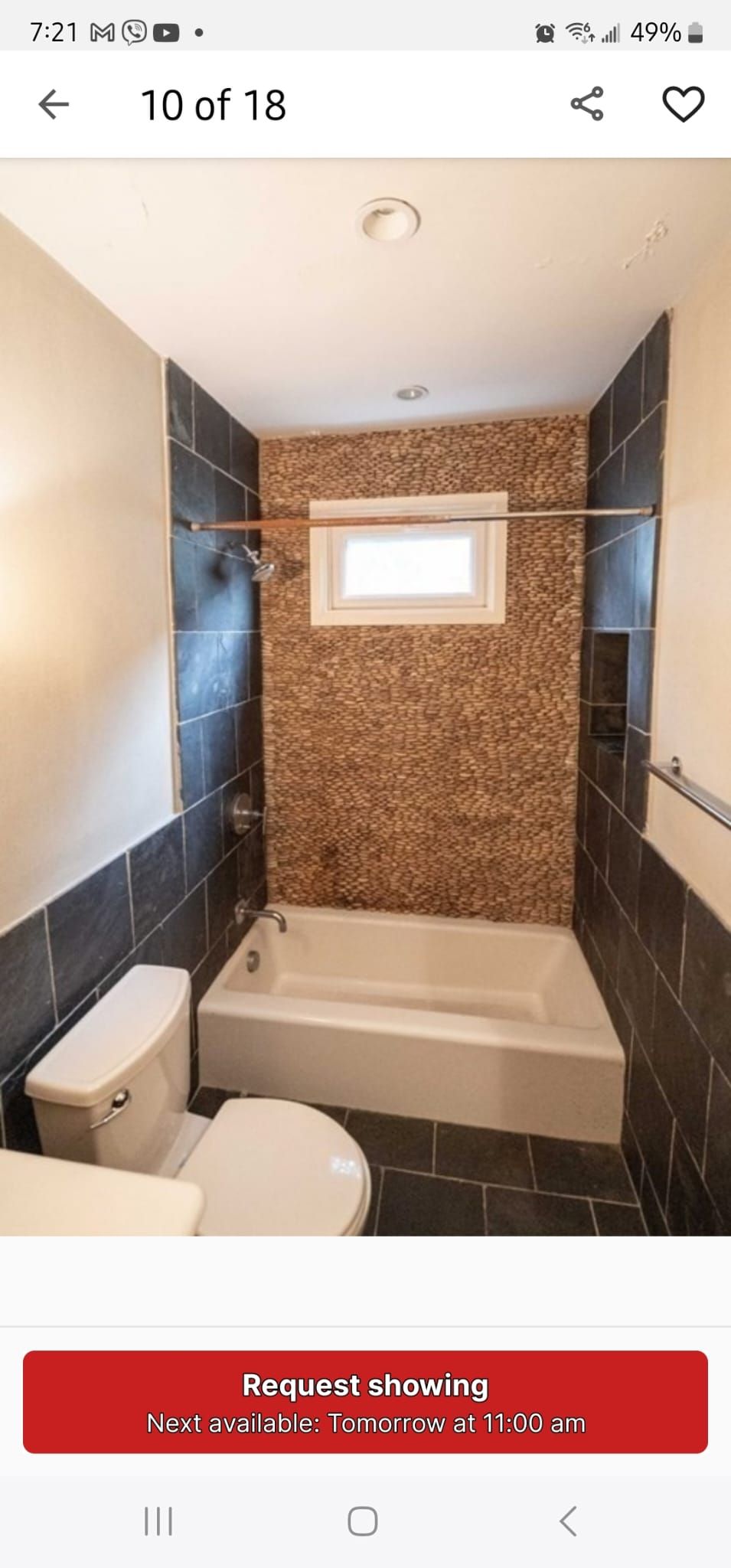 Modern bathroom with brick accent wall, bathtub, window, and toilet.