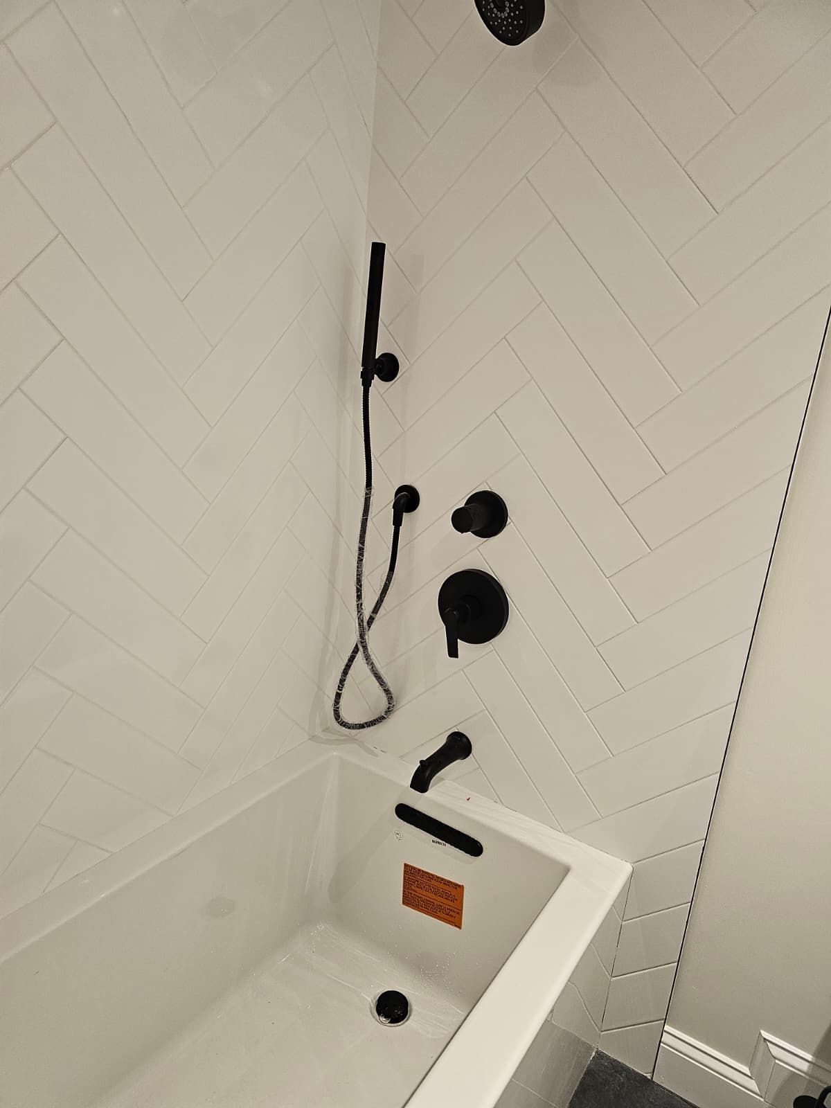 Modern white-tiled bathroom with a white bathtub and black shower fixtures