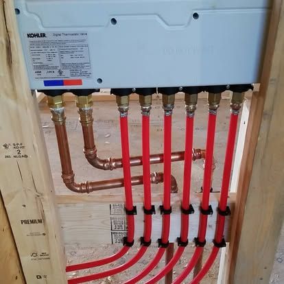 Piping manifold with red PEX tubes and copper pipes inside a wall cavity