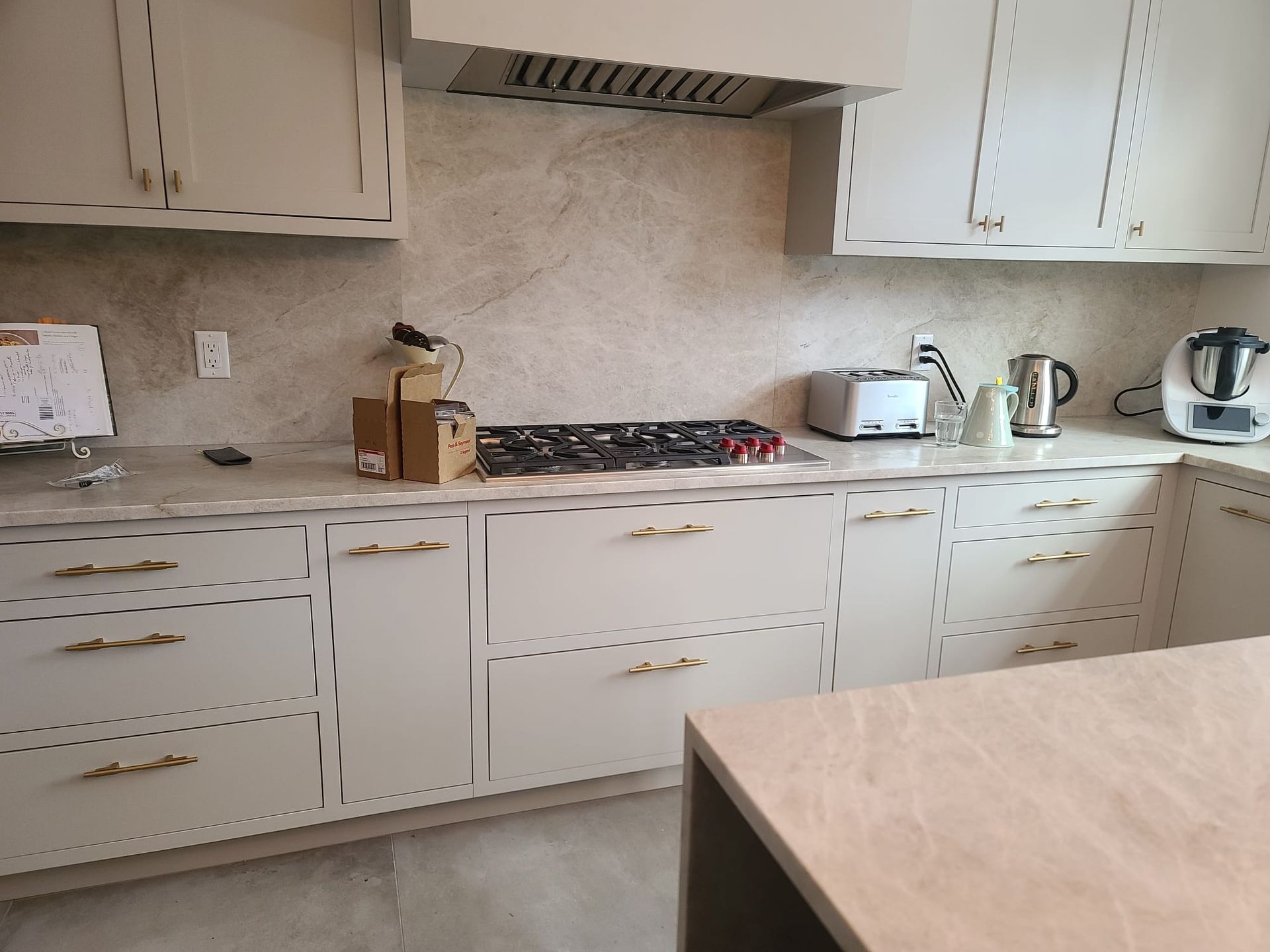 White kitchen counter with cabinets, toaster, kettle, stand mixer, and a marble tabletop in the foreground