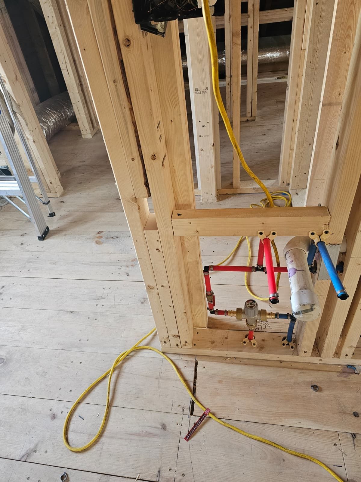 Open wall framing with exposed yellow, red, and blue plumbing lines and wiring in a construction site