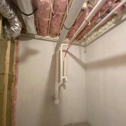 Basement utility room with exposed insulation, pipes, and framing on unfinished walls and ceiling.