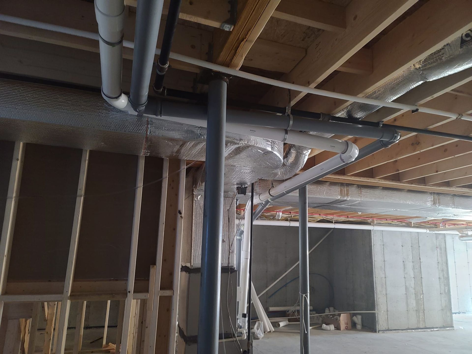 Basement construction with exposed ceiling beams, ductwork, and framing around a central metal support column.