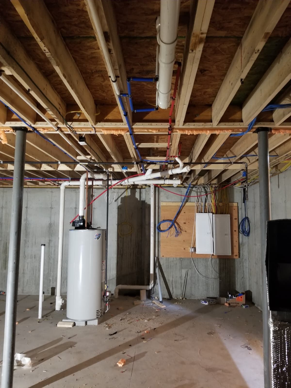 Basement under construction with exposed ceiling pipes, water heater, and unfinished walls.