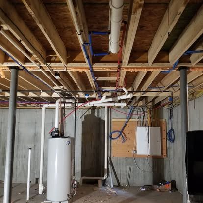 Unfinished basement with exposed ceiling beams, wiring, white water heater, and framed walls.