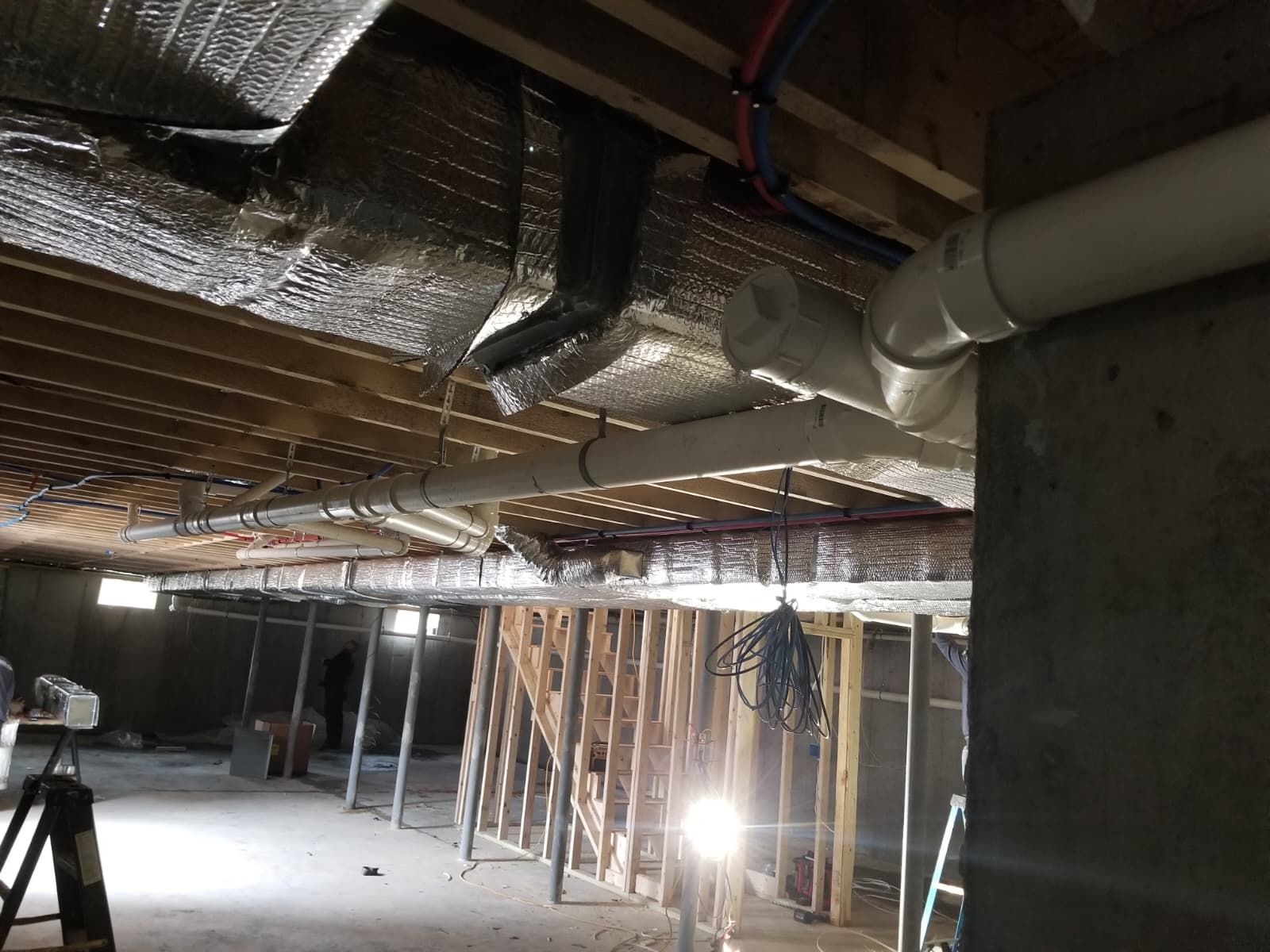 Unfinished basement with exposed insulation, framing, ductwork, and a bright work light.