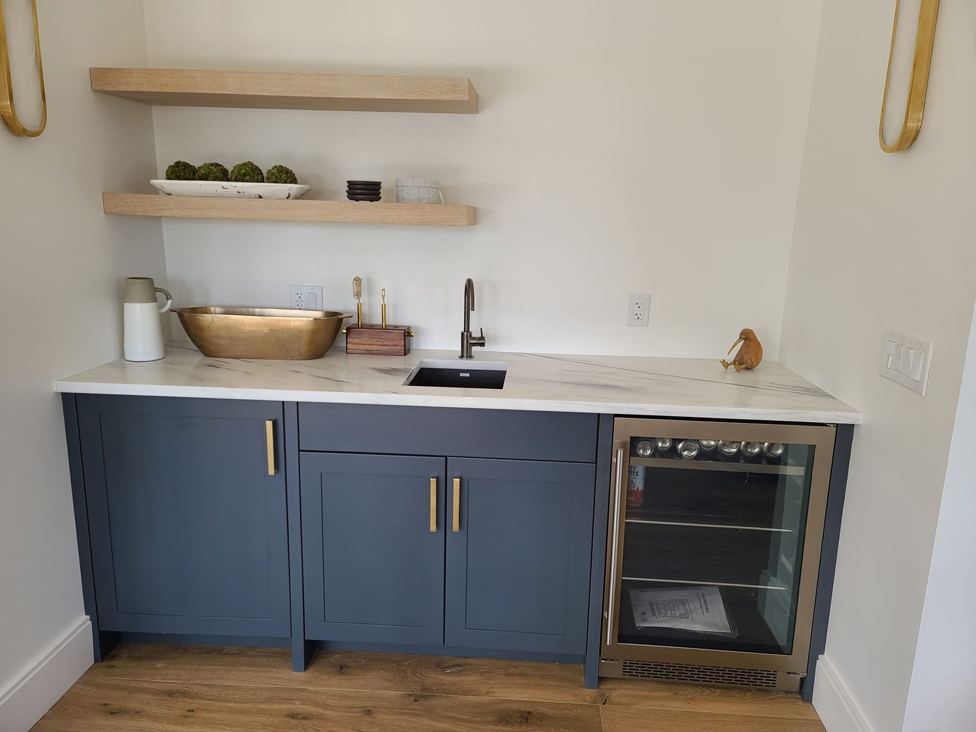 Small kitchen nook with blue cabinets, white countertop, wood shelves, and an undercounter beverage fridge.