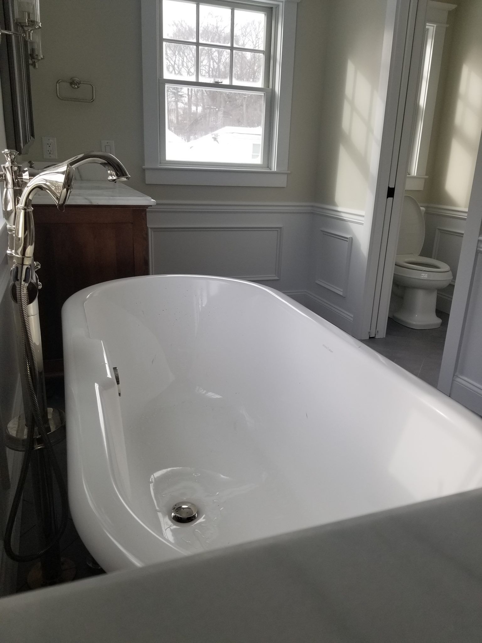 White clawfoot bathtub in a bright bathroom with a window and sink cabinet.