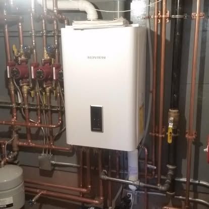 White wall-mounted water heater amid copper pipes in a utility room