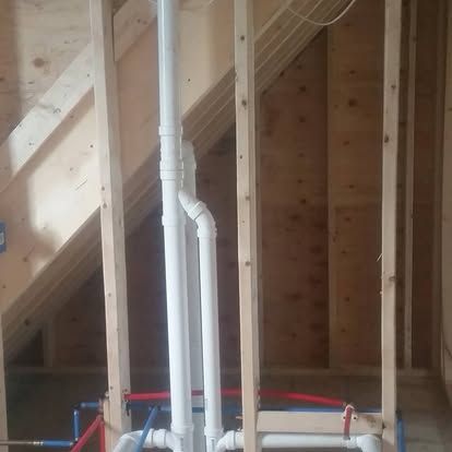 Exposed white PVC pipes and wooden framing inside an unfinished attic or wall cavity.