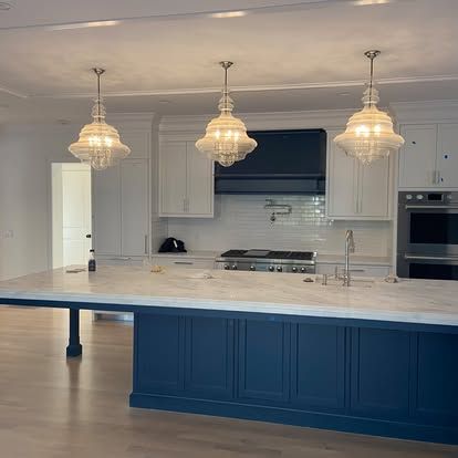 Modern kitchen with white cabinets, marble island, navy base, and three pendant lights