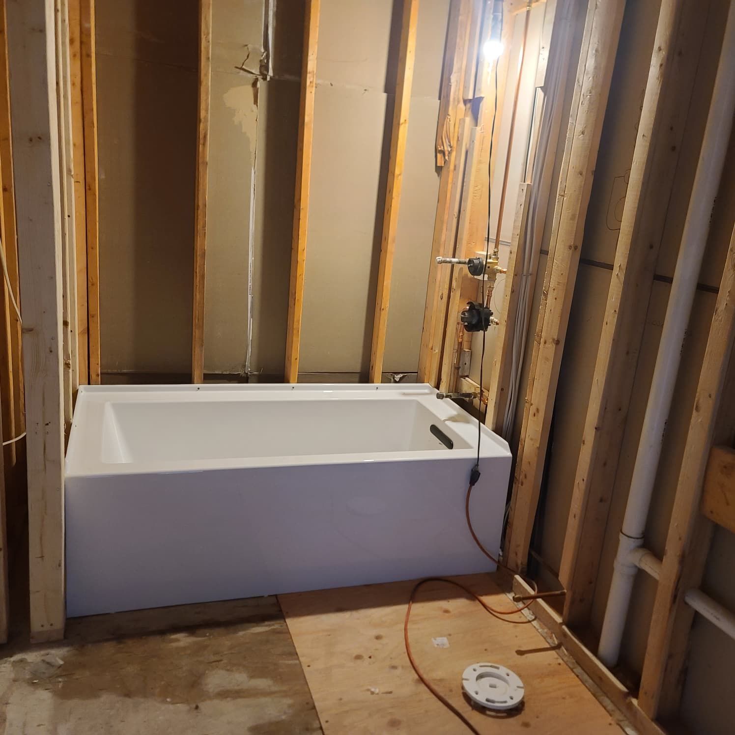 Unfinished bathroom with a white bathtub amid exposed wall studs and plumbing.
