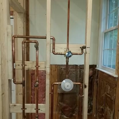 Exposed plumbing pipes and fixtures inside a partially stripped bathroom wall.