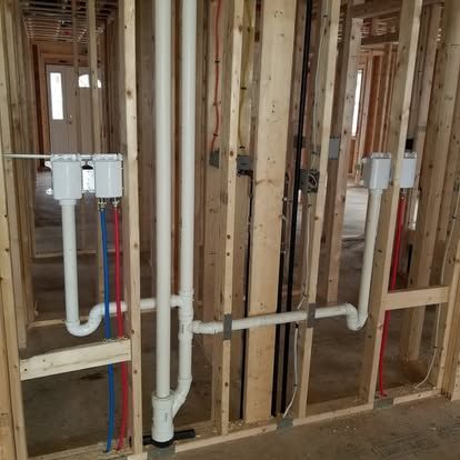 Framed interior wall with exposed plumbing pipes and valve boxes during home construction