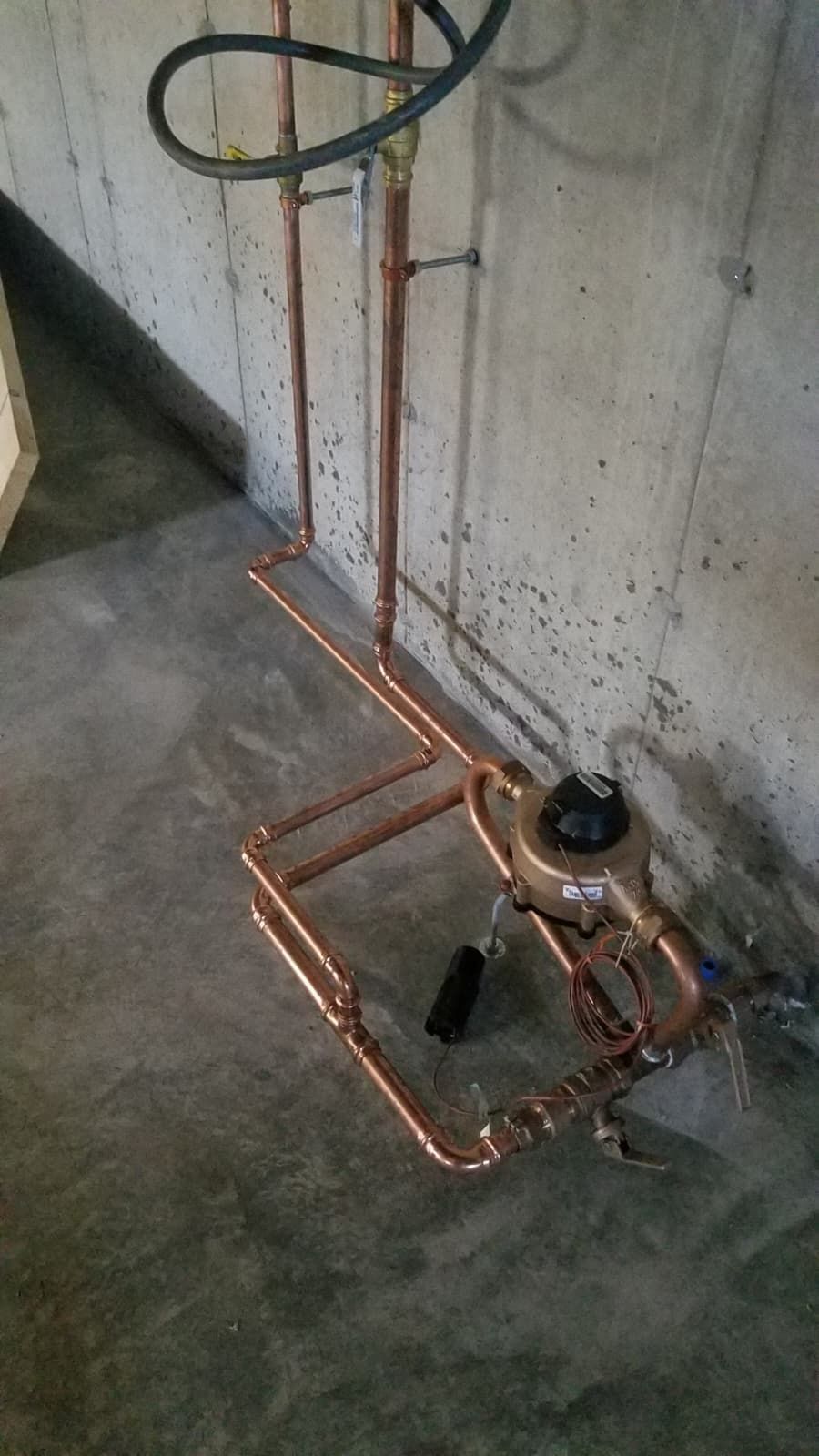 Copper pipe assembly with valves and tubing on a concrete floor against a wall.