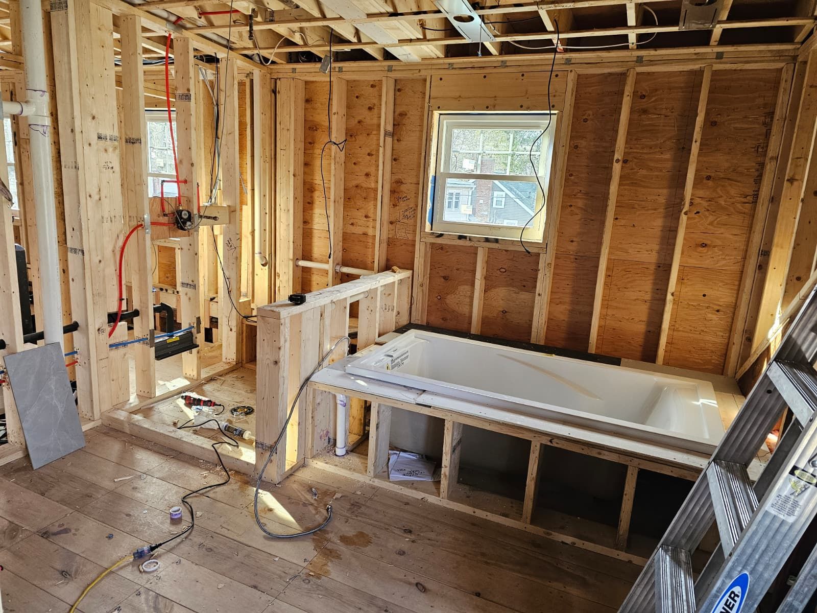 Unfinished house interior with exposed wooden framing, open walls, a window, and construction materials on the floor